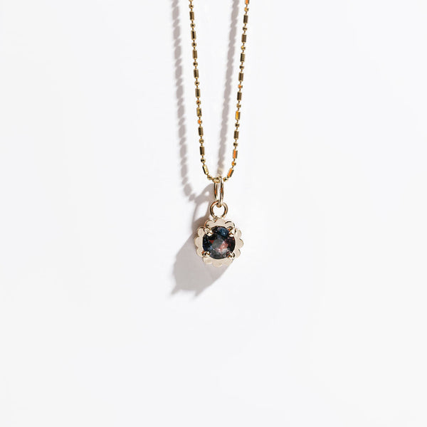 Gold necklace with a pendant featuring a dark purple and pink gemstone on a white background