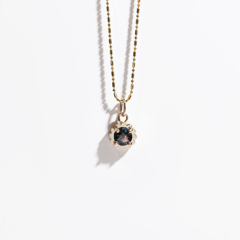 Gold necklace with a pendant featuring a dark purple and pink gemstone on a white background
